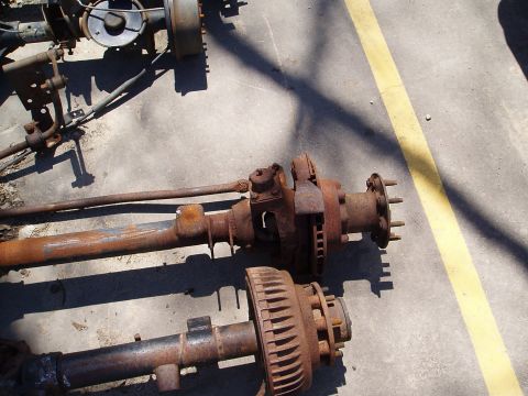 1978 Ford Bronco - Several rusty vehicle axles are laid out on a concrete surface with yellow lines.