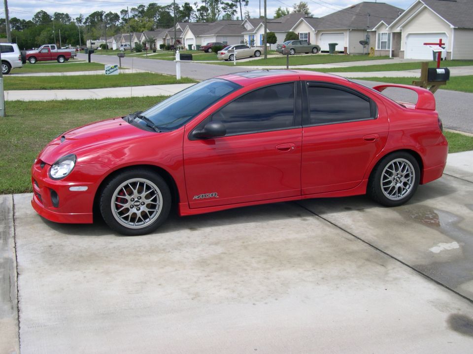Red compact sedan side profile with rear wing, side skirts and silver multi-spoke wheels