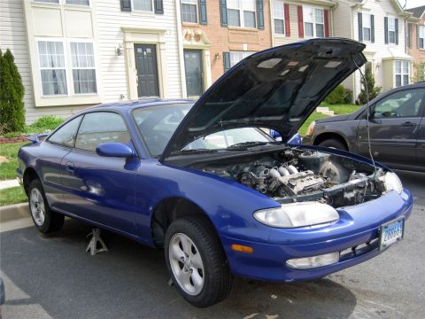 1993 Ford Probe - A blue coupe sits with its hood open, revealing the engine bay, while supported by jack stands.
