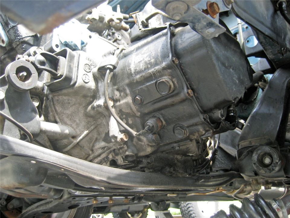 Underside view of a car's transmission and suspension parts, showing oil stains and rust