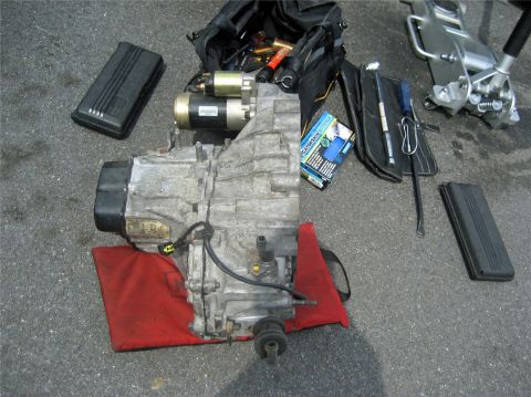 1993 Ford Probe - Car transmission and associated tools laid out on asphalt surface.
