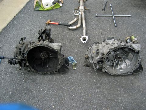 1993 Ford Probe - Car parts, including two transmissions and an exhaust manifold, are disassembled and placed on the ground.