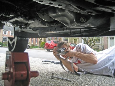 1993 Ford Probe - Man photographs car's underside while a red SUV is parked nearby.