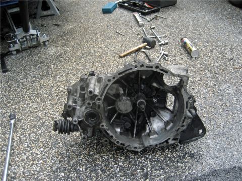 1993 Ford Probe - A car transmission is disassembled on the ground, surrounded by tools and automotive repair equipment.