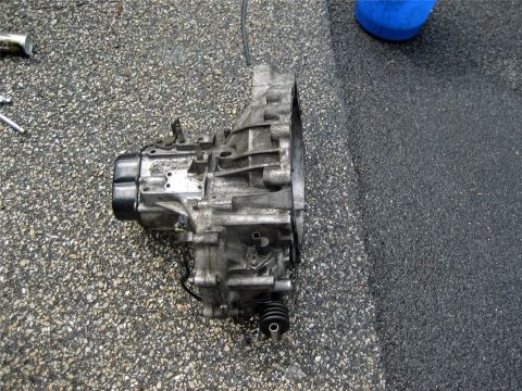 1993 Ford Probe - A transmission assembly rests on a textured asphalt surface, with visible metal components and a black rubber boot.