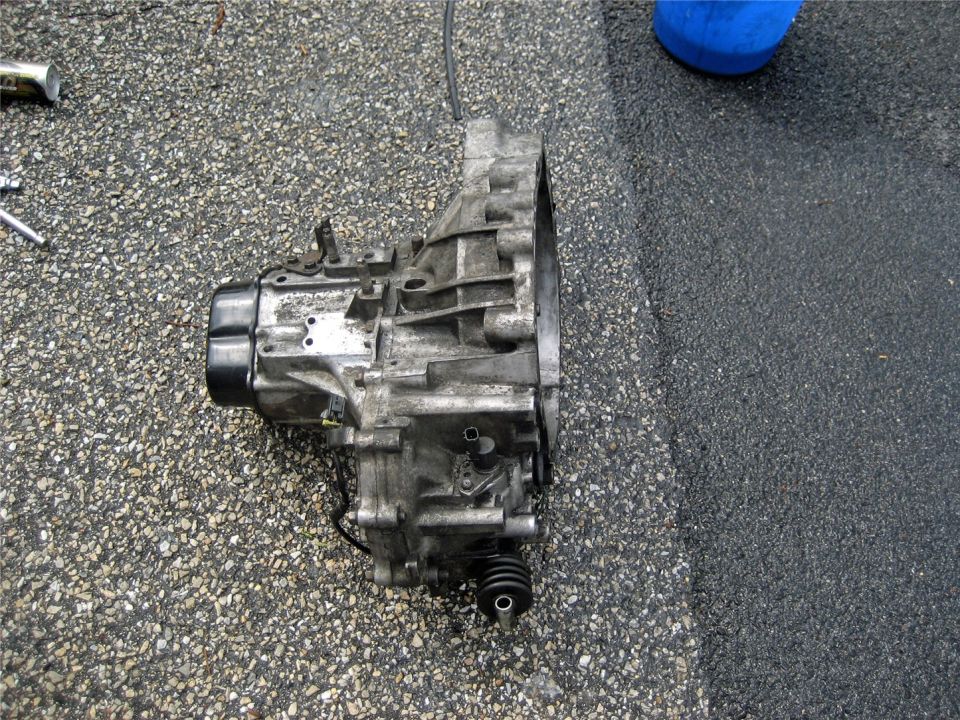 Transmission assembly on asphalt ground, showing metal casing and rubber boot