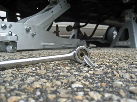 1993 Ford Probe - A ratchet lies on the ground next to a car supported by jack stands, suggesting maintenance work is underway.