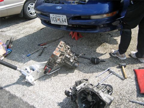 1993 Ford Probe - A blue 1993 Ford Probe is undergoing transmission repair with parts and tools laid out on the ground.
