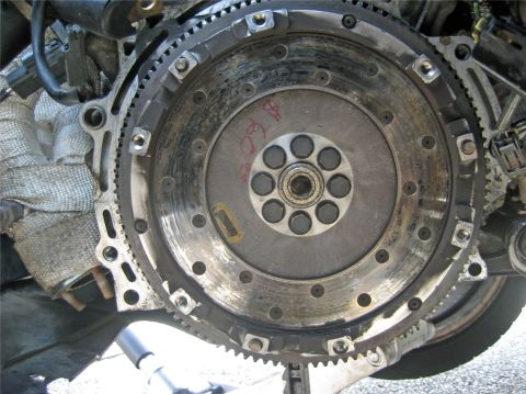 1993 Ford Probe - Close-up view of an engine flywheel, showing its gear teeth and central bolt pattern. Red markings are visible on the surface.
