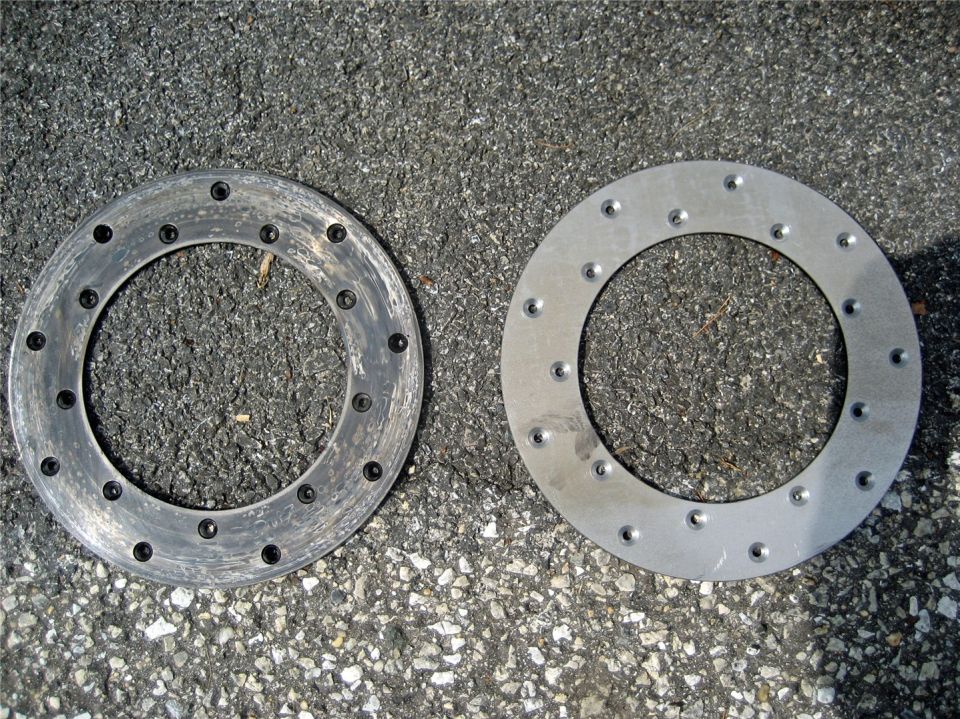 Two metal brake rotors, one used and one new, on asphalt
