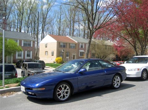1993 Ford Probe - A blue 1993 Ford Probe GT is parked on a residential street, with other vehicles and townhouses in the background.