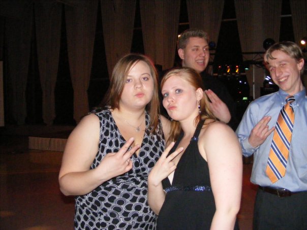 Four young adults pose for a photo, two women in front making peace signs, two men behind them. One man in a blue shirt and orange tie also makes a peace sign