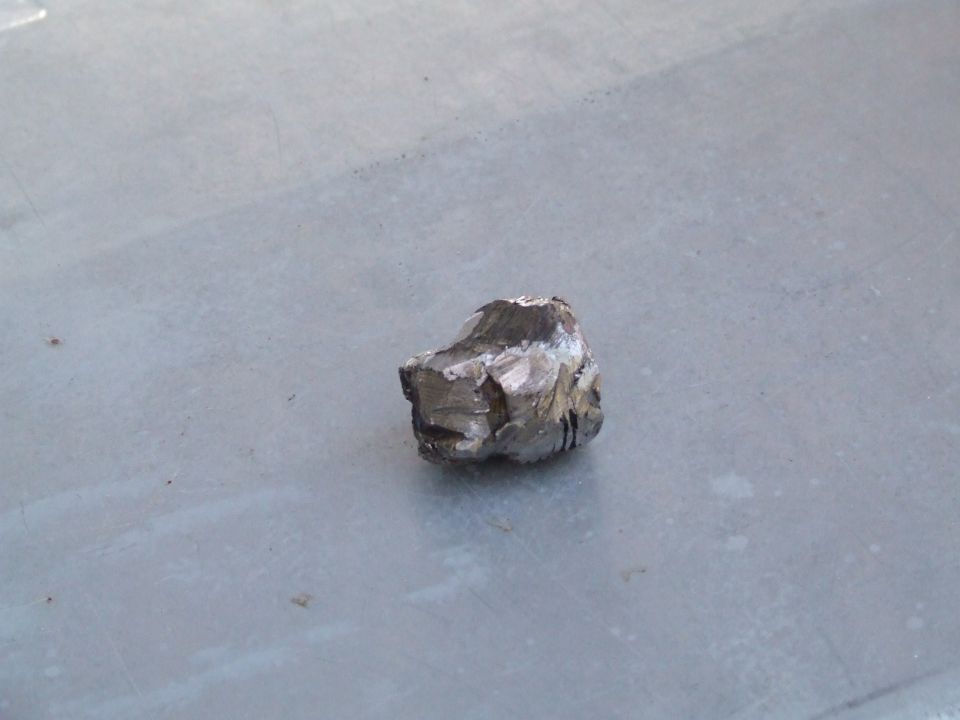 Fragment of broken metal with sharp edges, resting on a gray surface