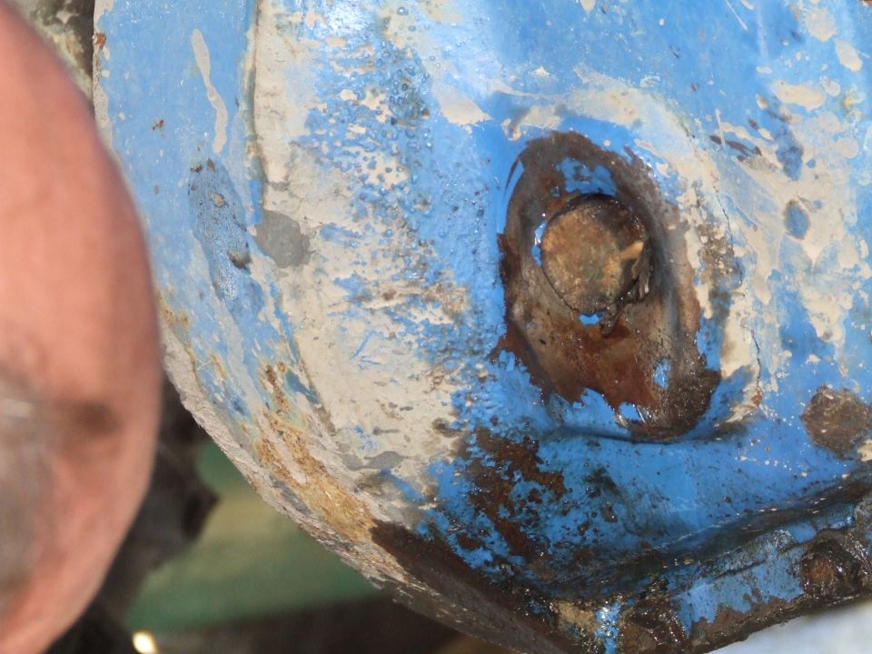 Close-up of a rusted metal component with peeling blue and white paint, showing a bolt head