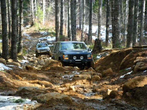 2005 Jeep Wrangler - Two Jeep Cherokee XJs tackle a challenging muddy and rocky off-road trail in a wooded area.