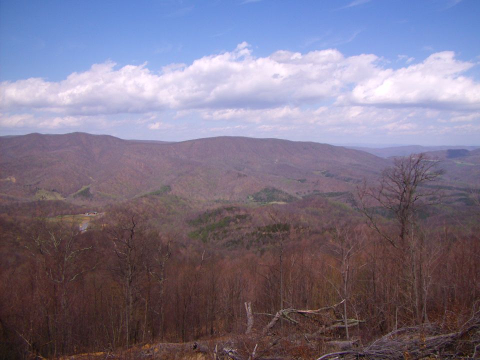 Mountain landscape with trees and a blue sky with clouds. Watermark reads SUPERMOTORS