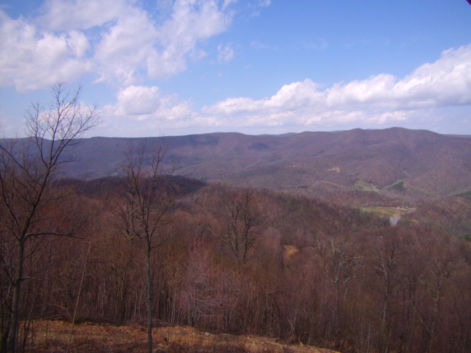 Mountain range under a cloudy blue sky, foreground with bare trees