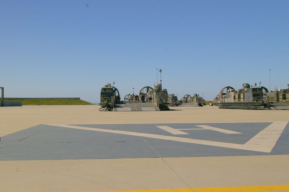 Several landing craft air cushions parked on a tarmac with a helipad marking in the foreground