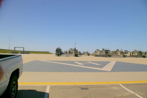 1986 Ford Bronco - A fleet of hovercraft landing craft are lined up on a sunny day, with a pickup truck in the foreground.