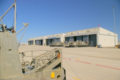 1986 Ford Bronco - Military hovercrafts are parked outside numbered hangars at a Navy facility under a clear blue sky.