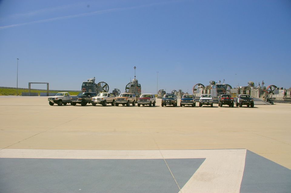 Line of SUVs and pickup trucks parked on a tarmac with hovercraft in the background