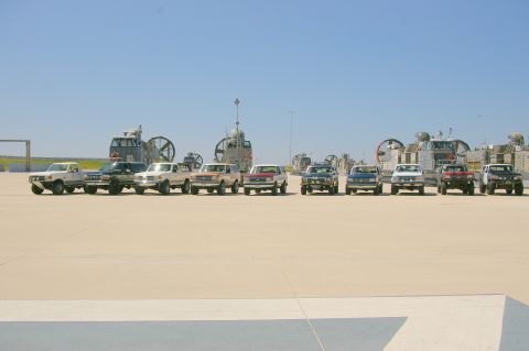 1986 Ford Bronco - Multiple Ford Broncos and F-Series trucks lined up with hovercraft in the distance.