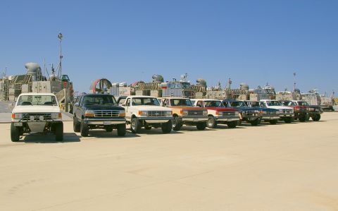 1986 Ford Bronco - A line of Ford pickup trucks are parked on a sandy lot with hovercraft in the background.