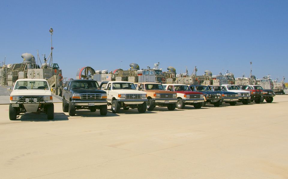 White Ford F-150 pickup truck with aftermarket bumper and lights, parked on sand