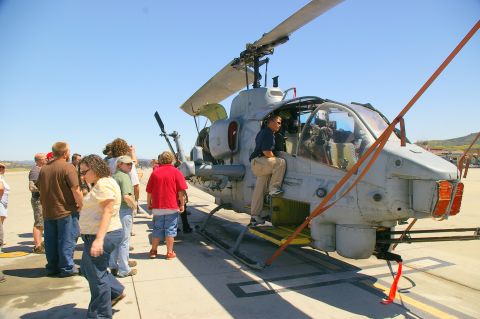 1986 Ford Bronco - A group of onlookers observe a military helicopter parked on an airport tarmac under a clear blue sky.