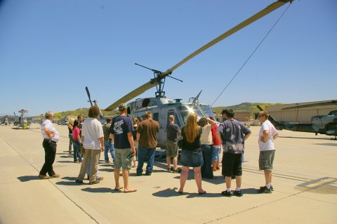 1986 Ford Bronco - A group of people observe a helicopter on a sunny day at an airfield event.