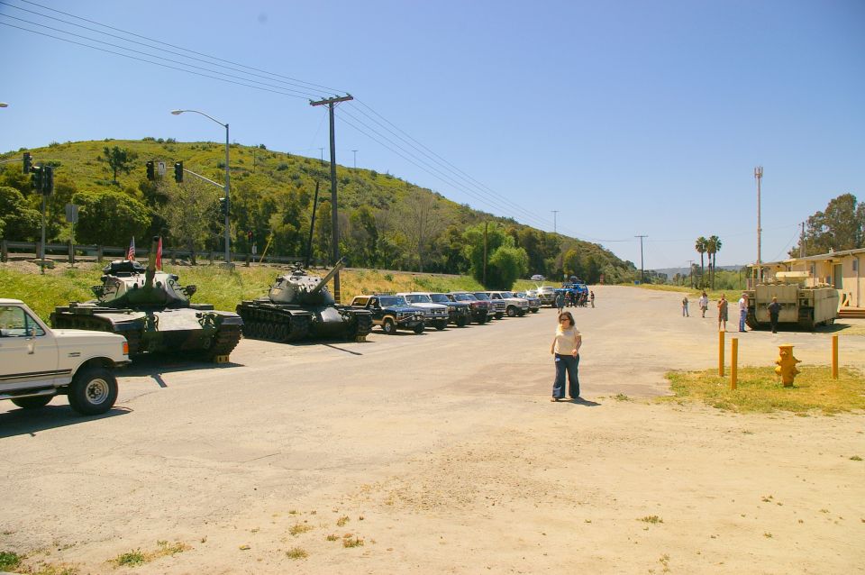 Two tanks and a line of parked trucks and SUVs on a sunny day