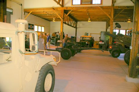 1986 Ford Bronco - Several military vehicles and equipment are displayed indoors, possibly in a museum or exhibition hall.