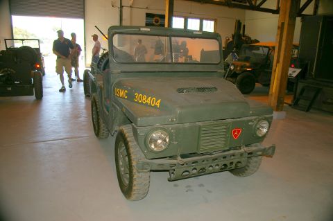 1986 Ford Bronco - Olive drab military jeep with USMC 308404 markings parked indoors with other vehicles.
