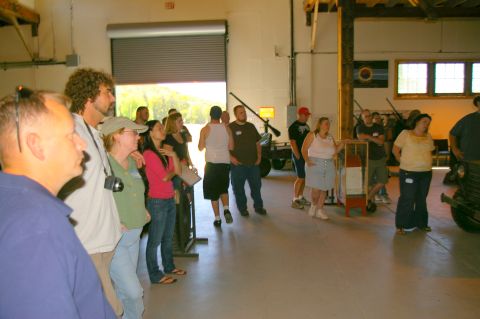 1986 Ford Bronco - A group of people are observing something in a large indoor space with an open garage door.