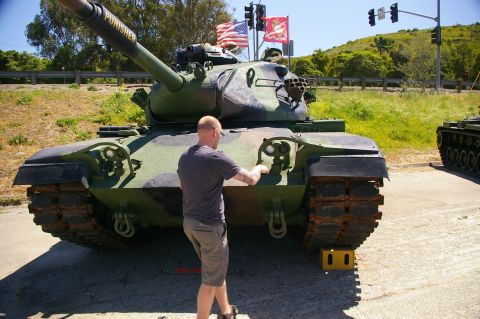 1986 Ford Bronco - A man inspects a military tank, which has the word 'PUNISHER' written on its cannon. Another tank is parked nearby.