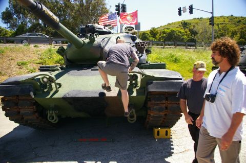1986 Ford Bronco - A man climbs onto a military tank, which has American and Marine Corps flags flying above it.