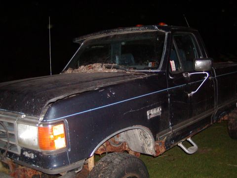 1991 Ford Bronco - This dark blue pickup truck is shown from a 3/4 front angle, revealing significant rust on its body and fender.