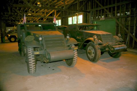 1986 Ford Bronco - Two military half-track trucks are parked inside a building, with a jeep in the background.