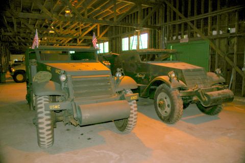 1986 Ford Bronco - Two vintage military half-track vehicles are parked indoors, one bearing USMC markings and a numerical identifier.