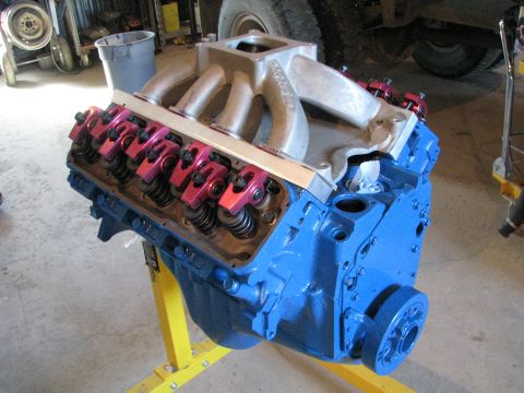1980 Ford F-250 - A blue V8 engine with an aluminum intake manifold and red roller rockers is displayed on a yellow stand.