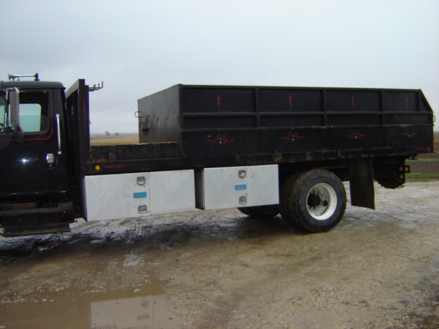 Side view of black flatbed truck with dual rear wheels and silver toolboxes
