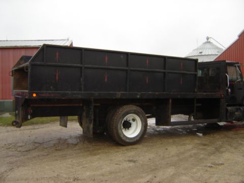 1992 Ford Bronco - A black flatbed truck with a tall cargo box is parked outdoors near farm buildings.
