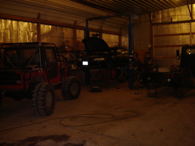 Modified off-road vehicle with roll cage and large tires in a garage, another vehicle on a lift behind it