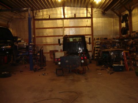 1992 Ford Bronco - A cluttered garage scene contains multiple vehicles undergoing maintenance or repair.