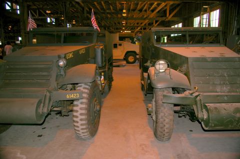 1986 Ford Bronco - Two military half-track vehicles are parked indoors, with a Humvee in the background.