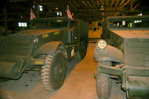 1986 Ford Bronco - Two military half-track vehicles are parked inside a large building, one with USMC markings.