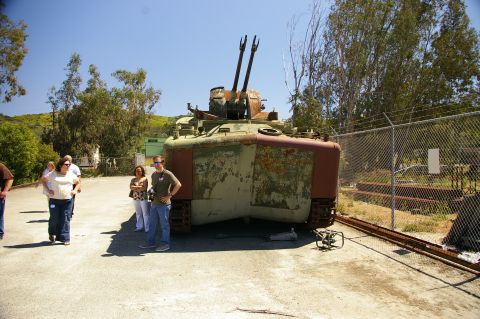 1986 Ford Bronco - An armored vehicle with twin cannons sits in an outdoor lot with people observing.