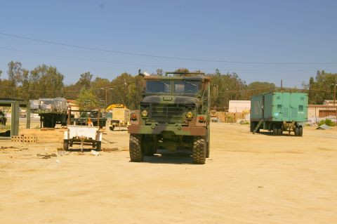 1986 Ford Bronco - A military truck is parked in an outdoor lot with other vehicles and trailers under a clear blue sky.