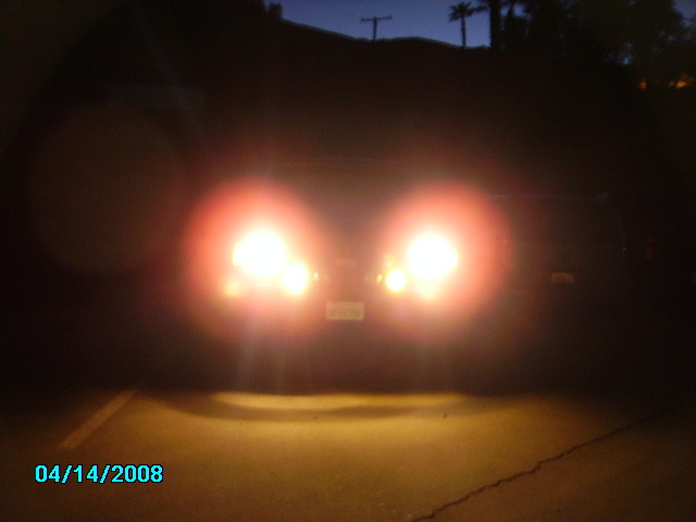 Rear of a dark vehicle with headlights on, license plate visible