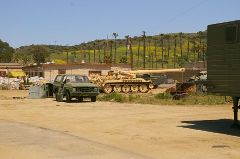 1986 Ford Bronco - A military scene with various vehicles and structures under a clear sky.